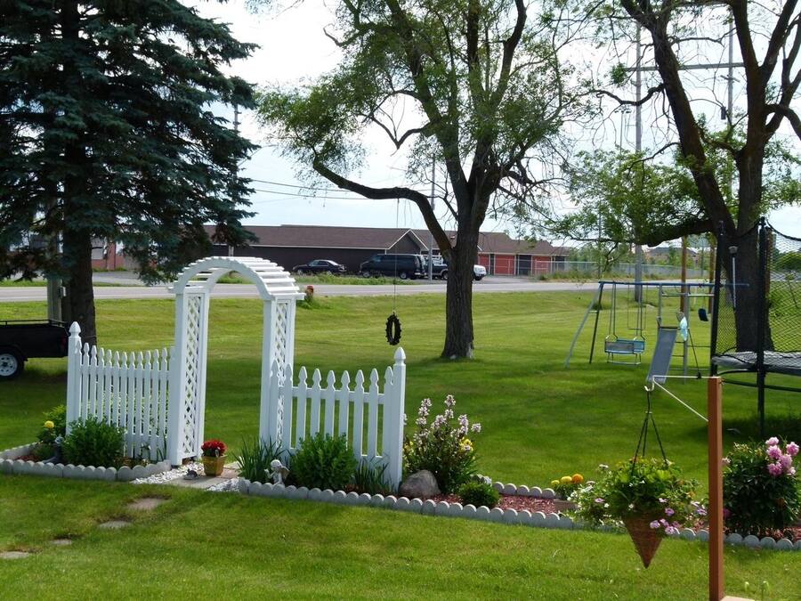 A residential lawn with a white picket fence, a swing set, and a gazebo.