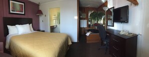 A hotel room with a bed, desk, chair, telephone, and television. - Country Squire Motel (Arnprior)