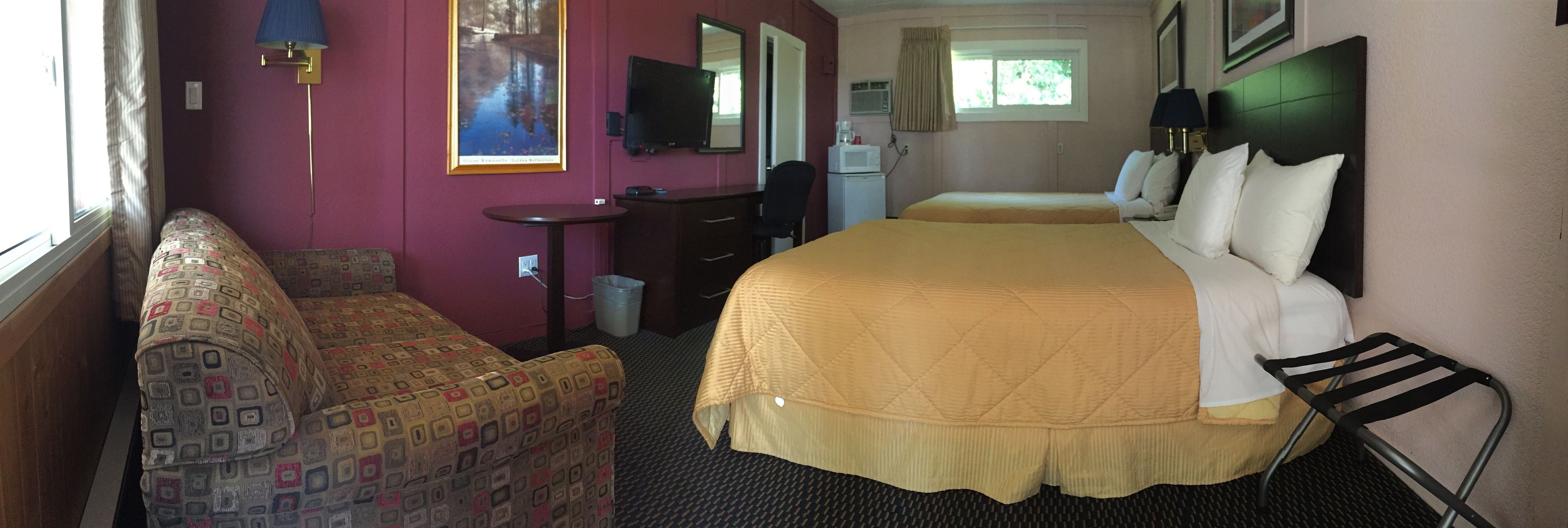 A hotel room with two beds, a desk, a chair, a television, and a window.