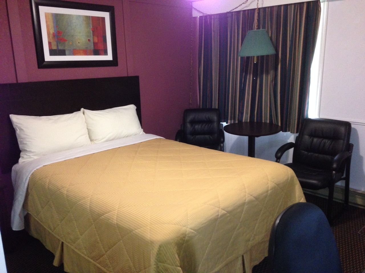 Une chambre d’hôtel avec un lit, deux chaises, une table et un tableau au mur.