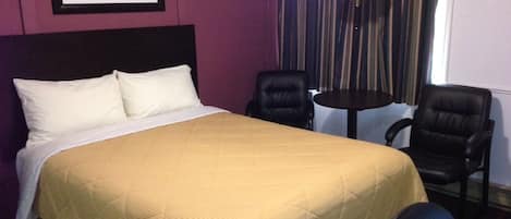 Habitación de hotel con cama, dos sillas, una mesa y un cuadro en la pared.