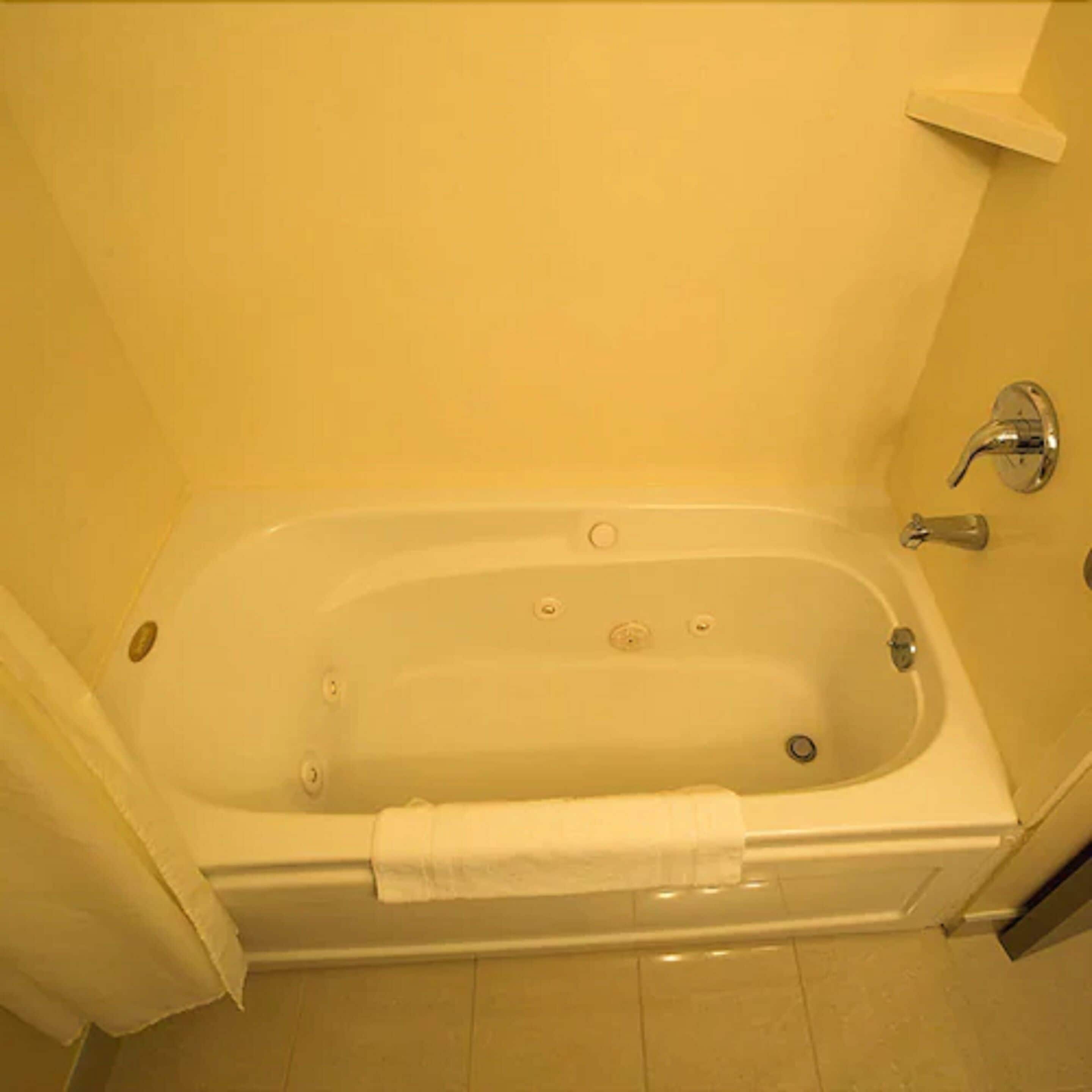 A standard bathtub with a faucet and a showerhead, a towel hanging on the side, and a door leading to the bathroom.