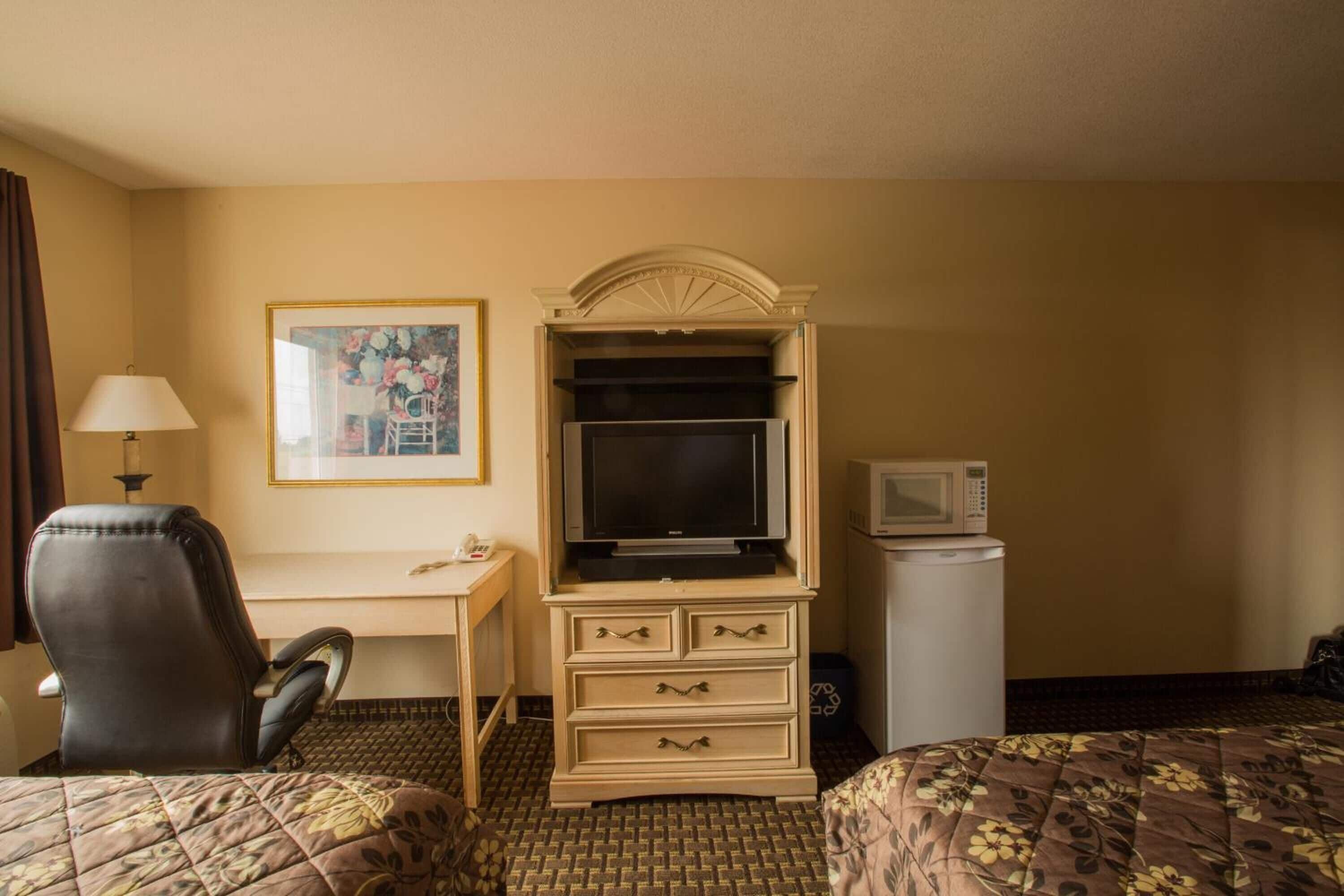 A hotel room with a bed, a desk with a television, a microwave, and a chair.