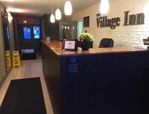 A reception area with a wooden counter, a sign for 'The Village Inn', and a 'Ring Bell For Assistance' sign. - The Village Inn (Centre Wellington)