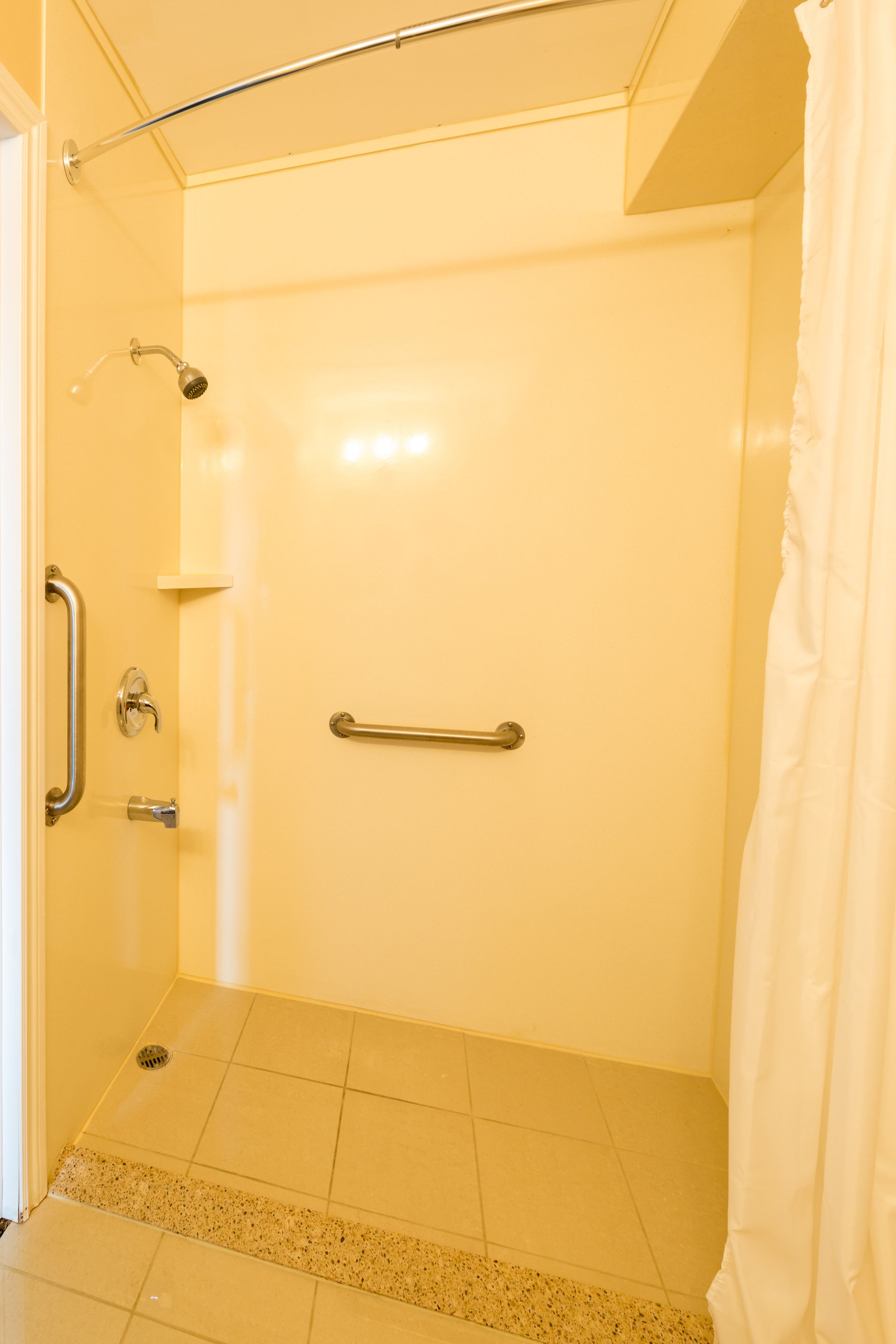 A bathroom with a shower, grab bars, and a white curtain.