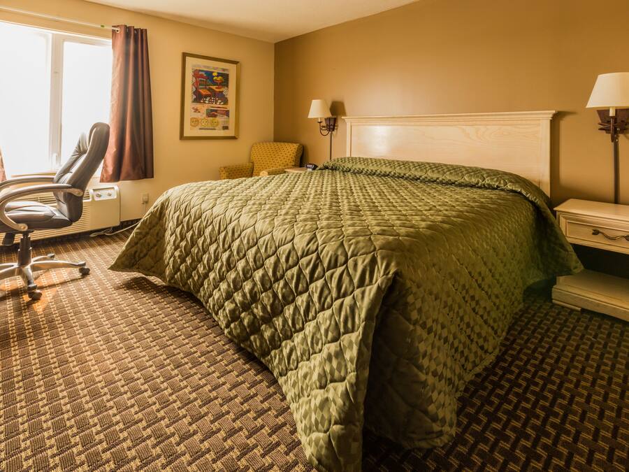 A hotel room with a large bed, a chair, a nightstand, and a lamp.
