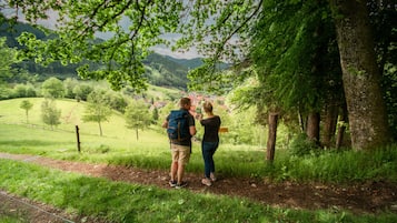 Una pareja parada en un sendero de tierra rodeada de vegetación exuberante, con vistas a un pueblo y colinas a lo lejos.