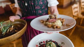 Una persona sosteniendo dos platos de comida: uno con un guiso de carne y patatas, y otro con un postre.