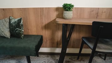 A wooden bench with a woven plant pot, a dark green upholstered bench, and a black chair in a room with patterned carpet.