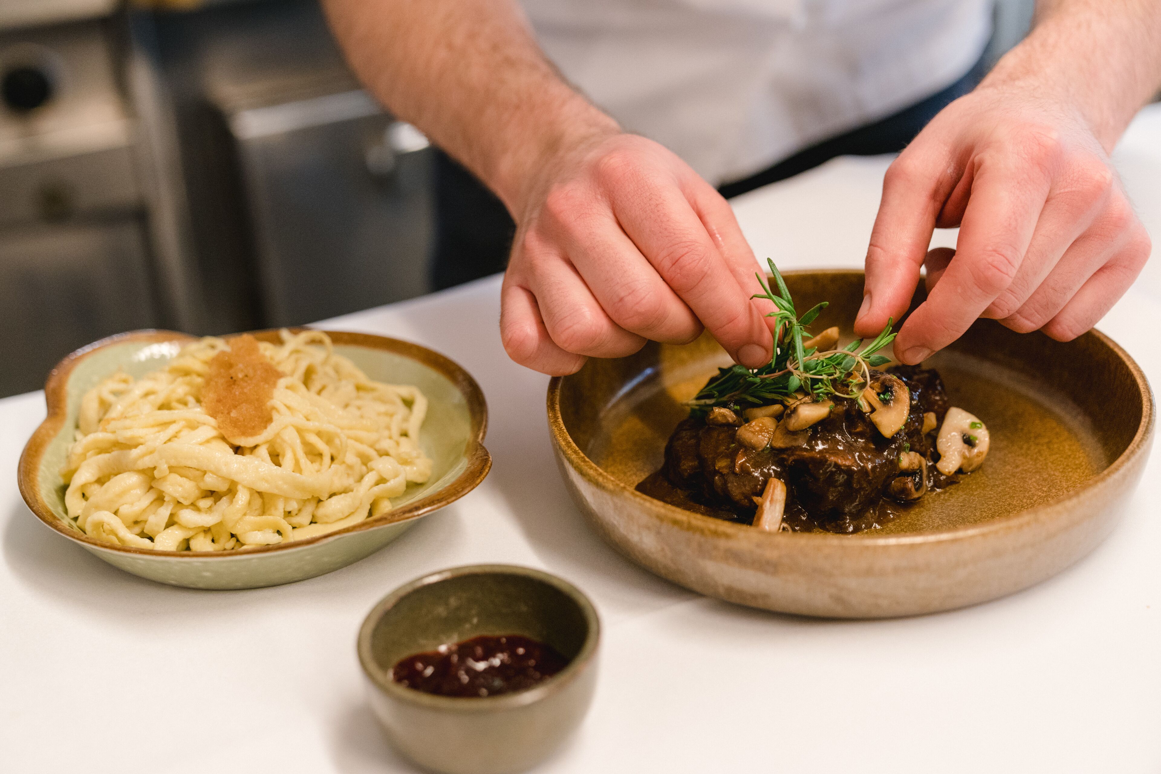 Un chef adornando un plato con hierbas.