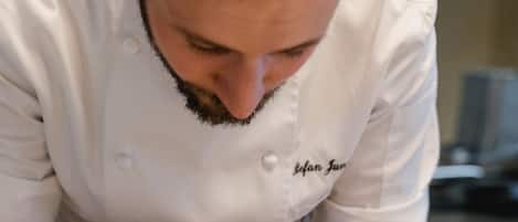 Un chef preparando un plato con una fuente negra, un vaso de salsa y una variedad de verduras.