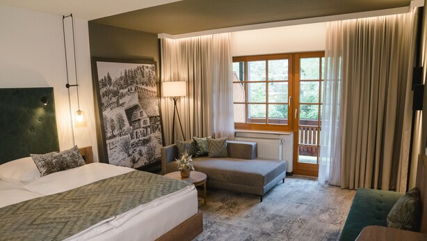 A hotel room with a large bed, a sofa, a small table, and a window with curtains. - Landhotel Hirschen (Oberwolfach)