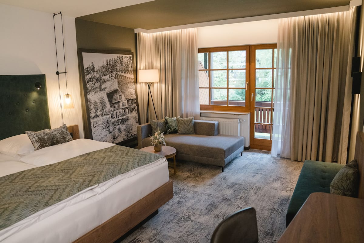A hotel room with a large bed, a sofa, a small table, and a window with curtains.