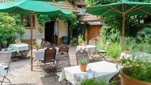 An outdoor patio with tables and chairs, covered by green umbrellas, surrounded by potted plants and greenery. - Landhotel Hirschen (Oberwolfach)