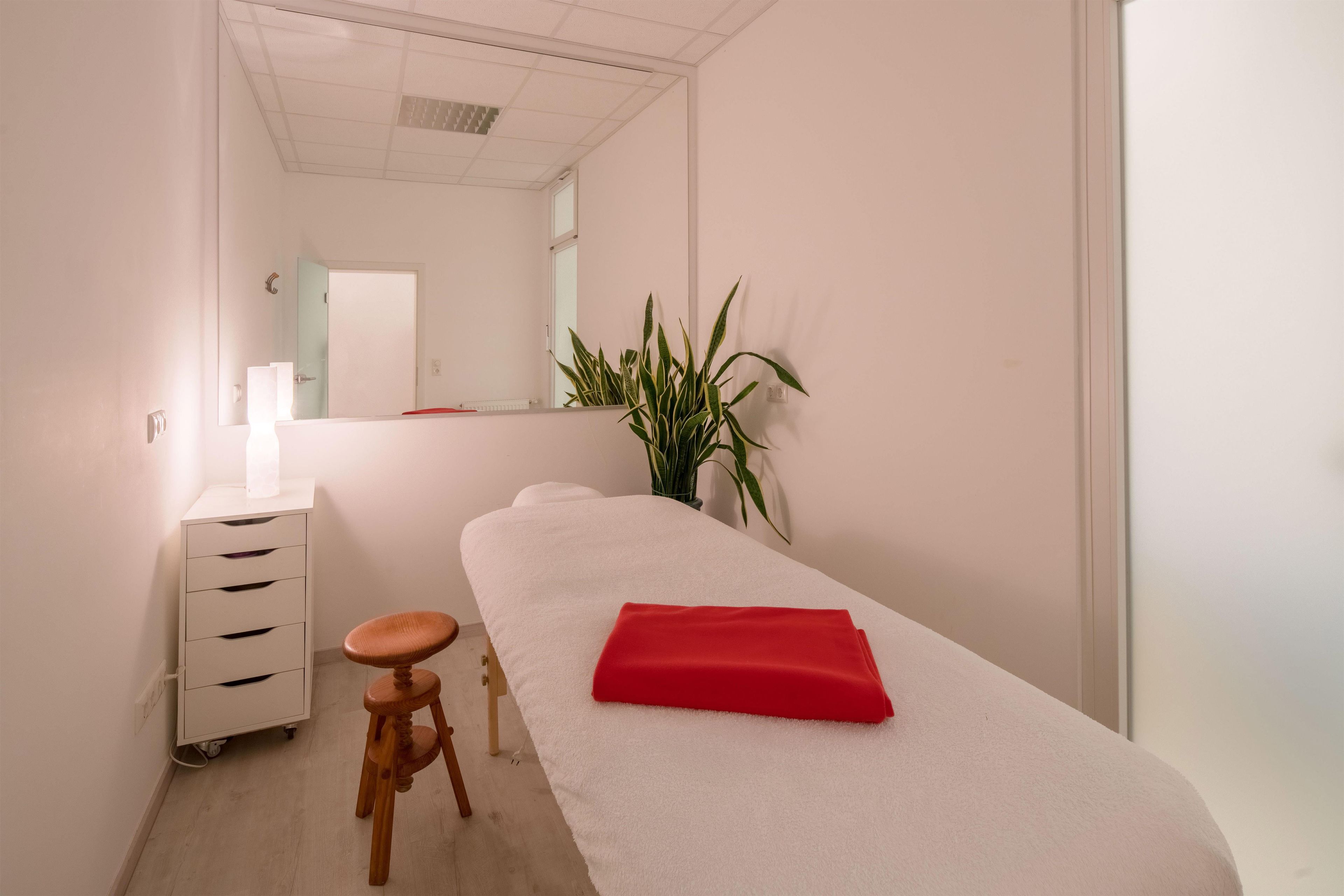 A spa room with a massage table, a wooden stool, a white cabinet, and a potted plant.