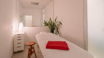 A spa room with a massage table, a wooden stool, a white cabinet, and a potted plant.