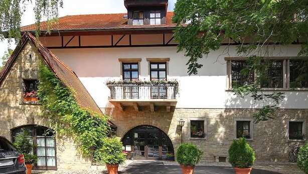 A stone building with a traditional design, featuring a central archway entrance, a balcony with railings, and potted plants. - Best Western Hotel Polisina (Frickenhausen a. Main)