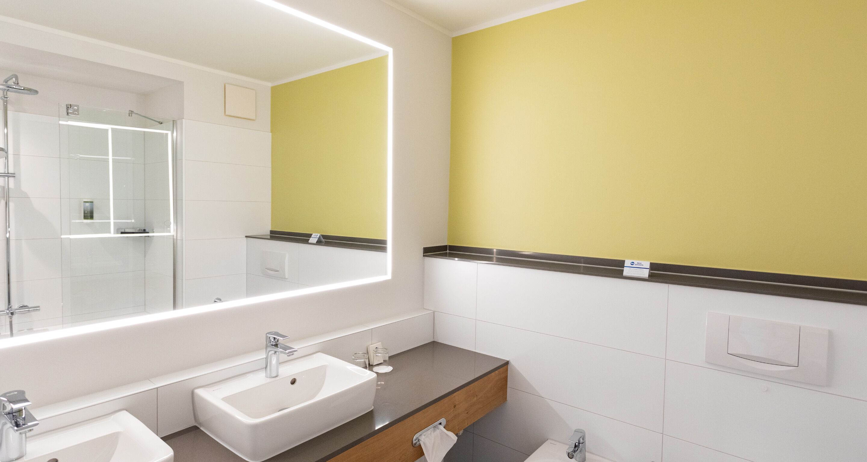 Un baño moderno con dos lavamanos, un espejo grande y una ducha.