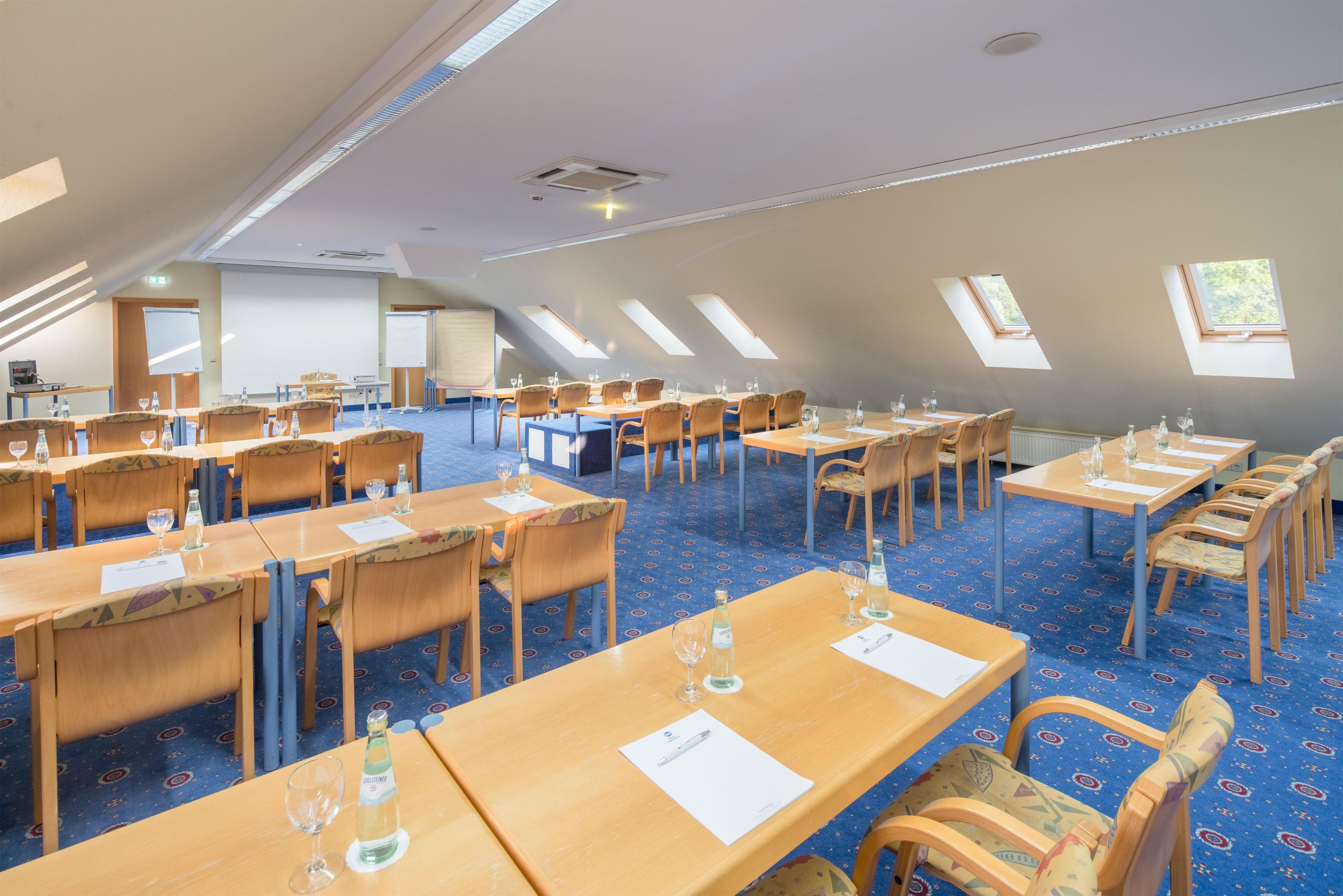 Un salón de conferencias con varias mesas y sillas, equipado con proyectores y pantallas.