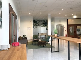 Um lobby moderno com balcão de atendimento em madeira, área de estar e um grande mural na parede.