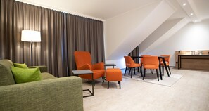 A modern hotel room with a green sofa, orange chairs, a small table, and a desk with a lamp. - Best Western Hotel Polisina (Frickenhausen a. Main)