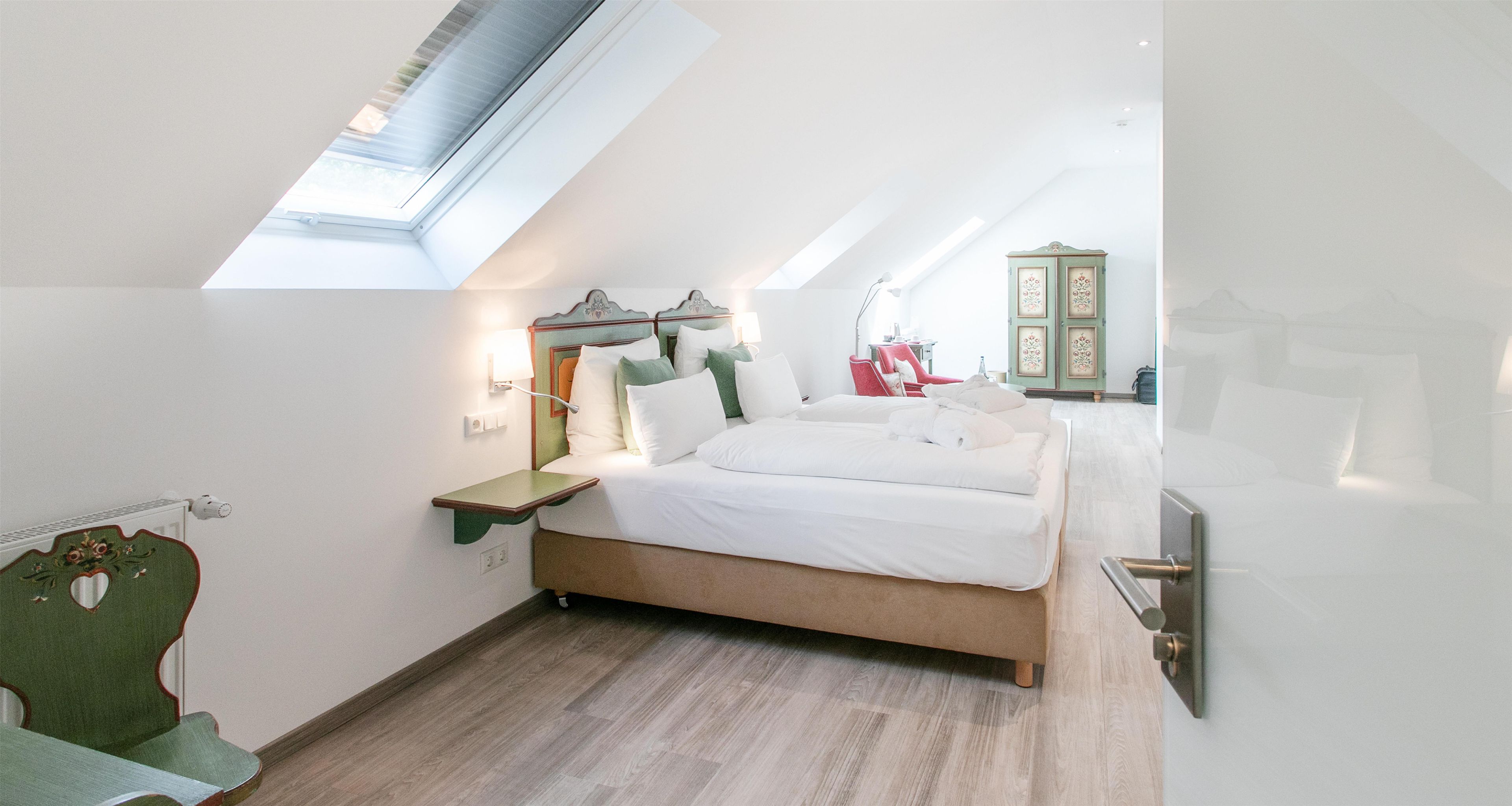 Un dormitorio con tragaluz, cama con ropa de cama blanca, mesita de noche, silla y armario.