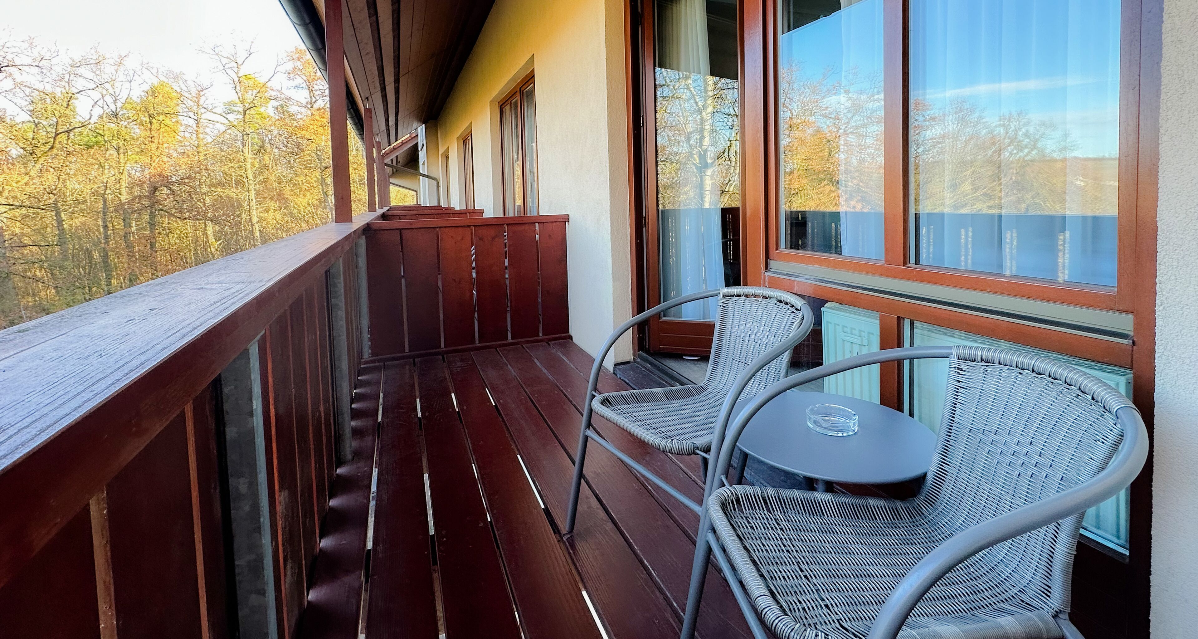 Ein Balkon mit Holzgeländern, Korbstühlen und einem kleinen Tisch.