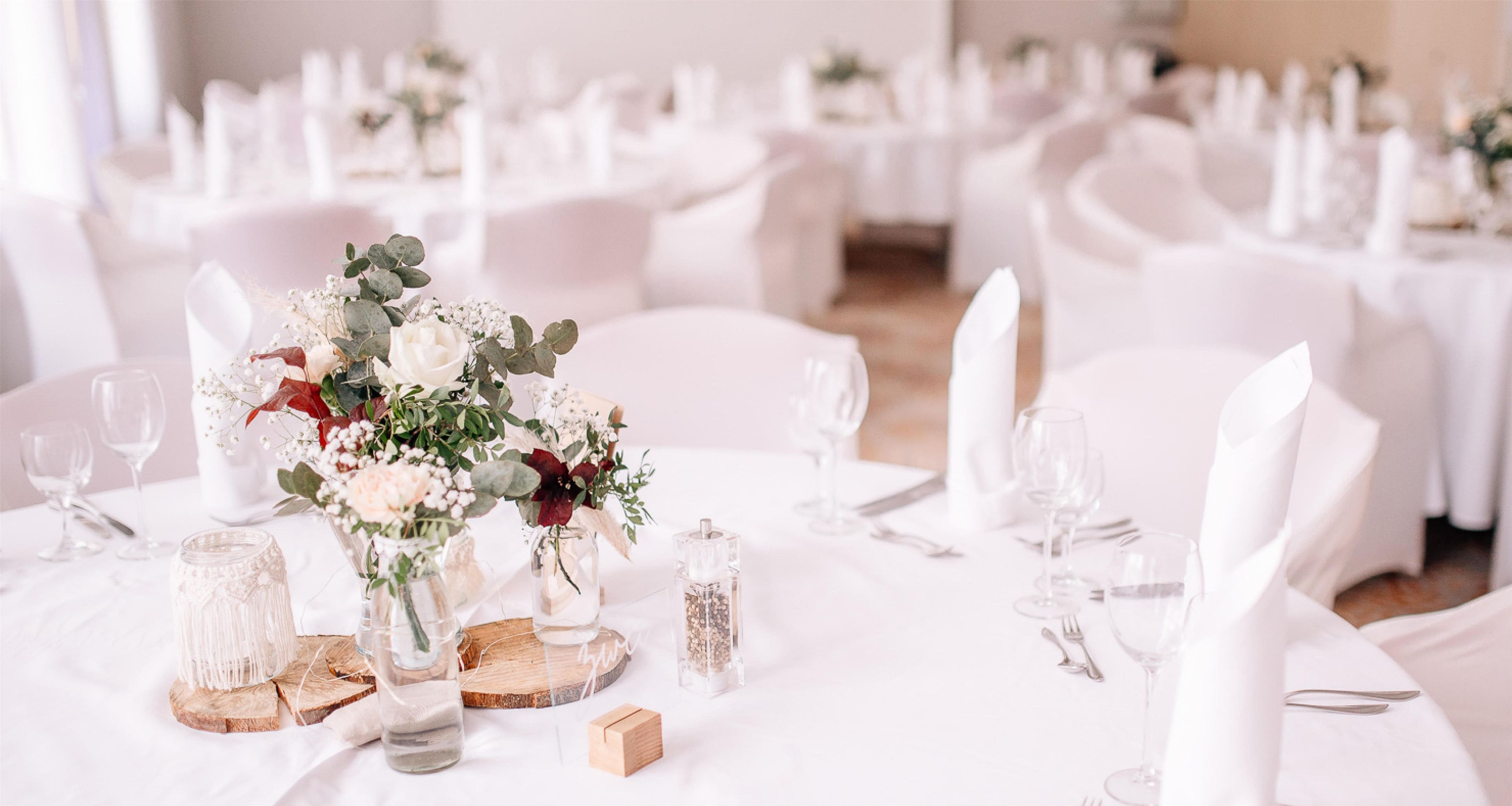 Une salle de banquet avec des tables rondes dressées pour un événement formel, agrémentées de compositions florales et recouvertes de nappes blanches.