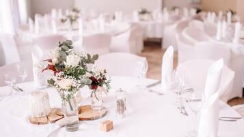 Une salle de banquet avec des tables rondes dressées pour un événement formel, agrémentées de compositions florales et recouvertes de nappes blanches.
