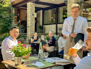 A patio area with stone pillars, outdoor seating, and a person pouring a drink. - Best Western Hotel Polisina (Frickenhausen a. Main)
