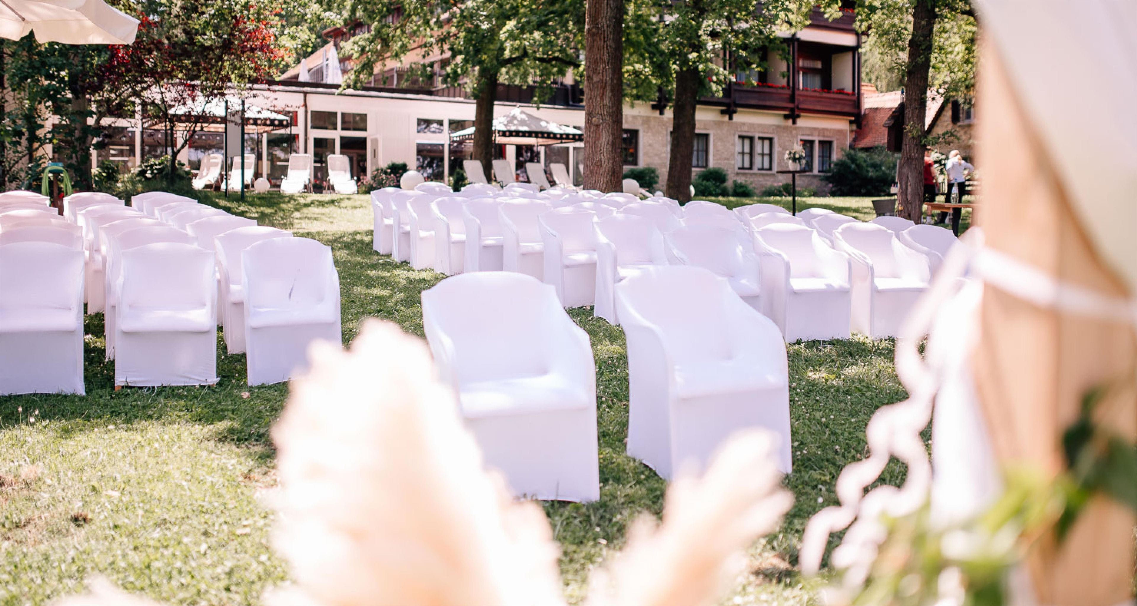 Rows of white chairs arranged outdoors, likely for an event, with a building in the background.