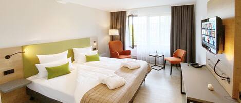 Une chambre d’hôtel avec un grand lit, deux fauteuils, un bureau et une télévision.
