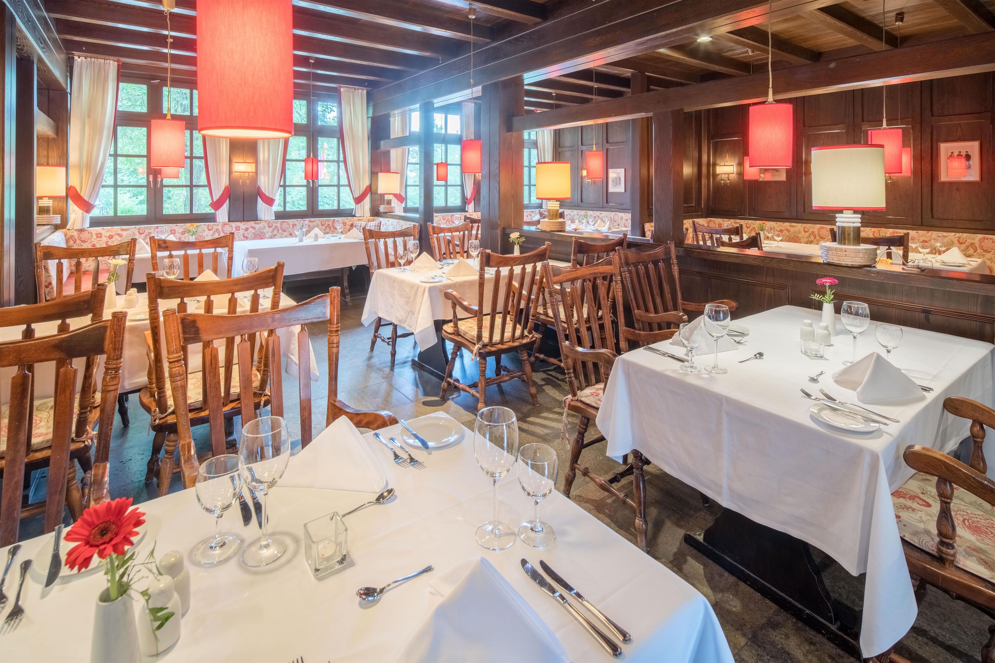 A restaurant interior with wooden furniture, white tablecloths, and red pendant lighting.
