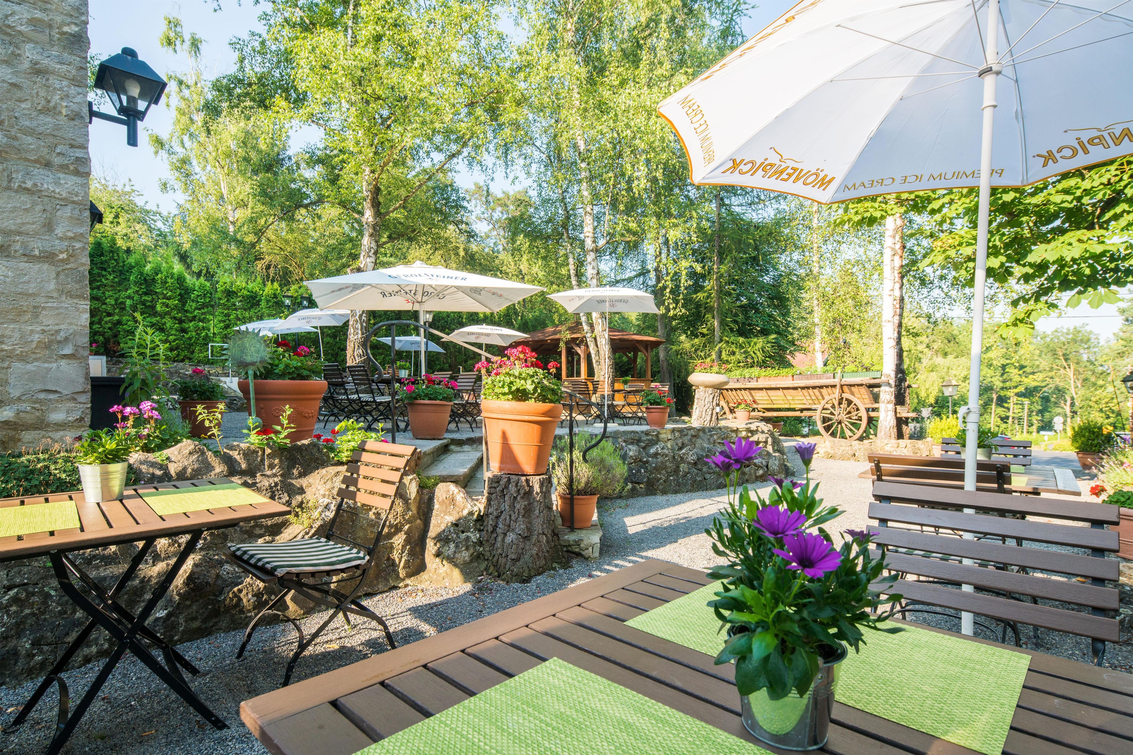 An outdoor seating area with tables and chairs, surrounded by potted plants and umbrellas.