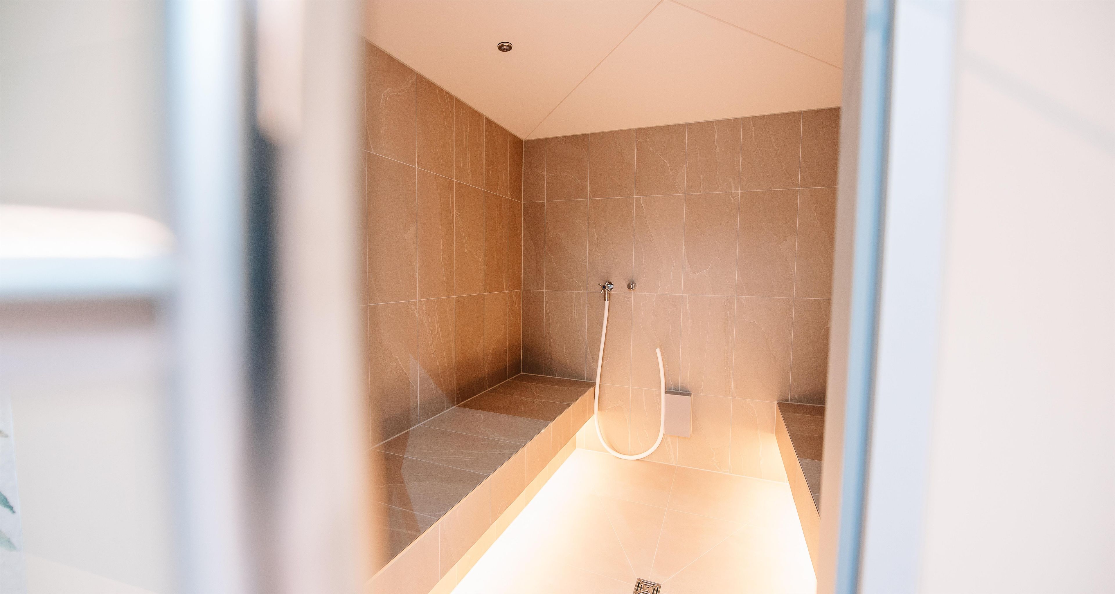 Un baño moderno con zona de ducha, paredes revestidas de azulejos y ducha visible.