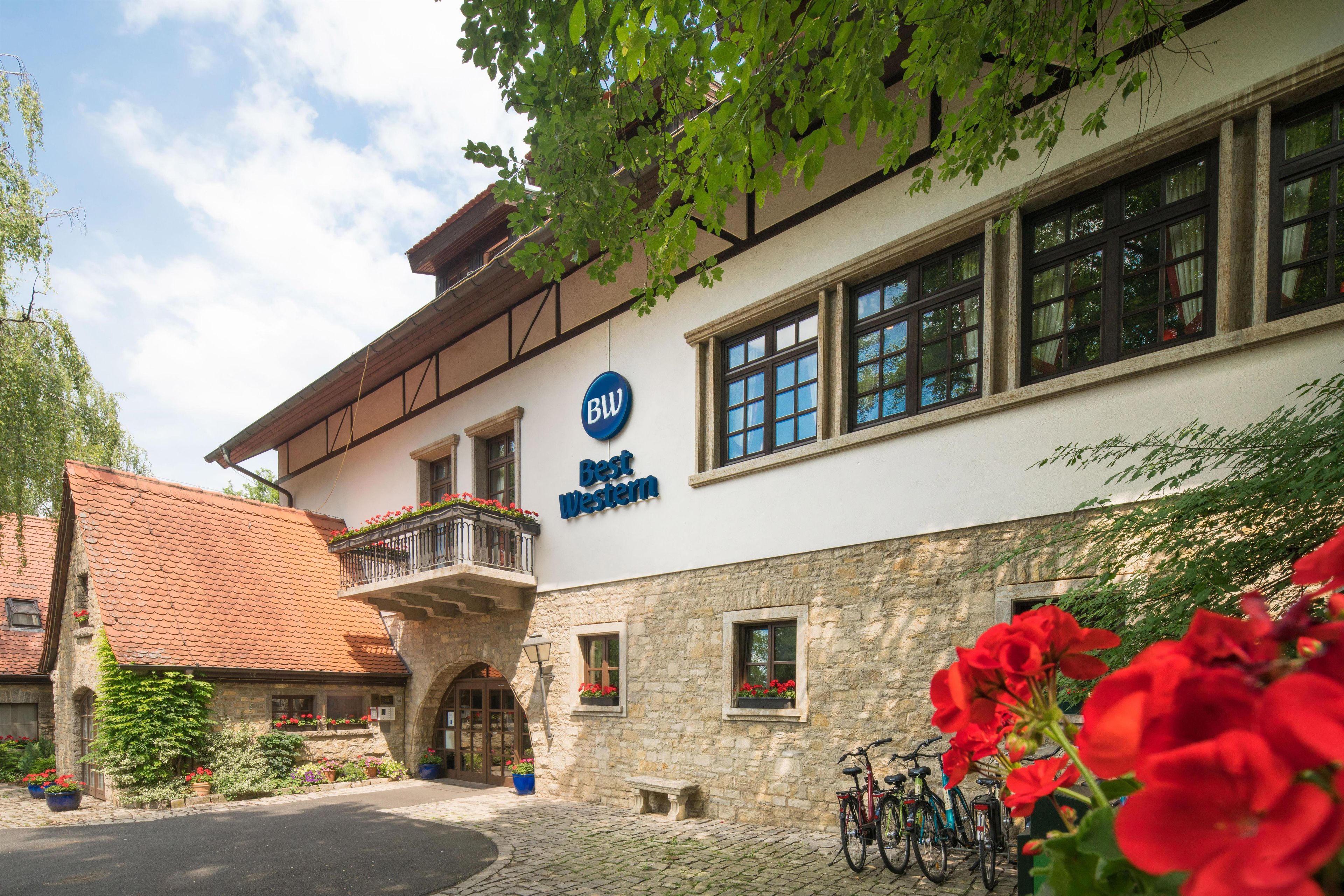 A hotel with a stone facade, a balcony with flowers, and a sign that reads 'Best Western.'