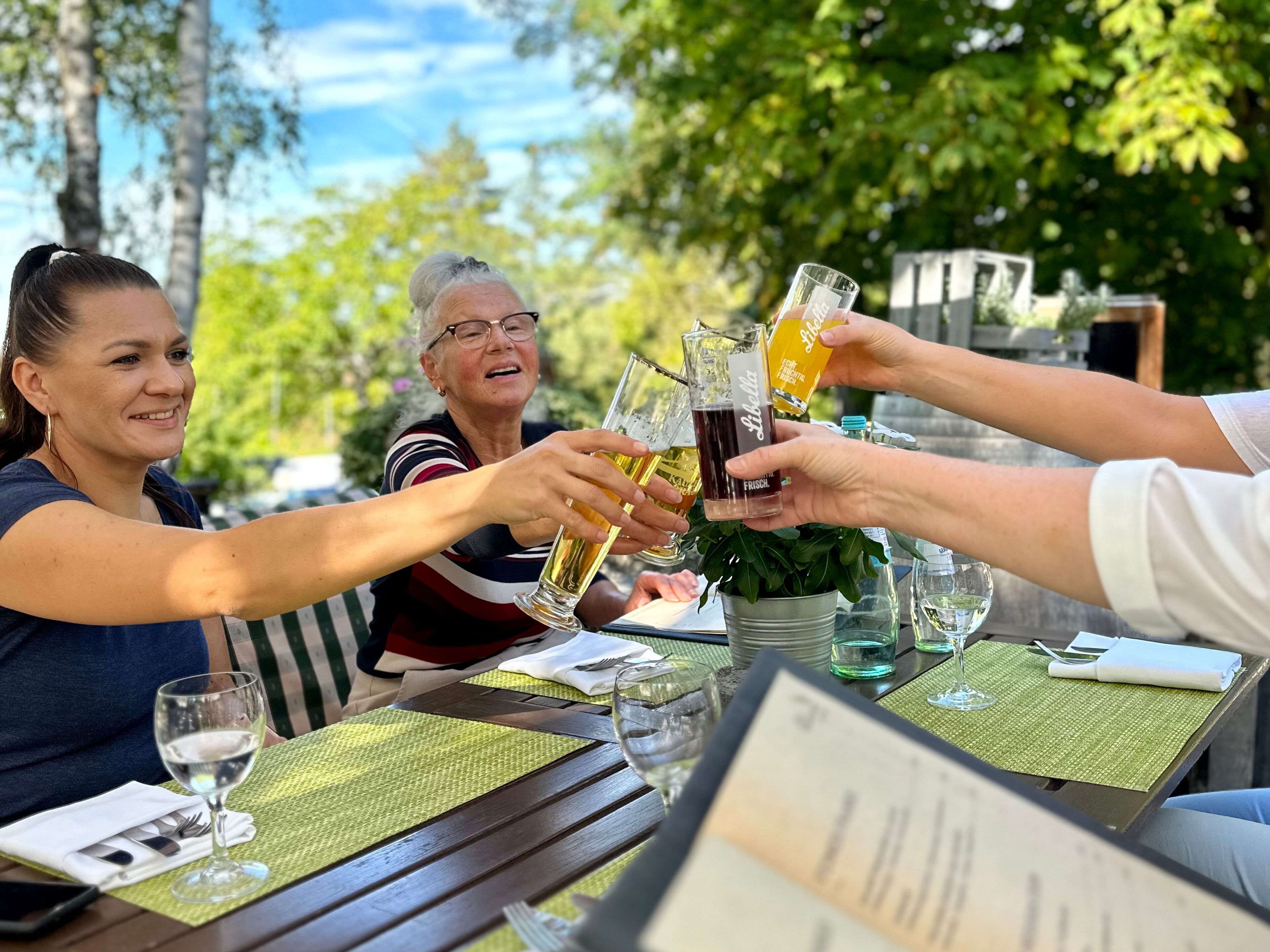 A group of people toasting with drinks at an outdoor table with a menu in front.