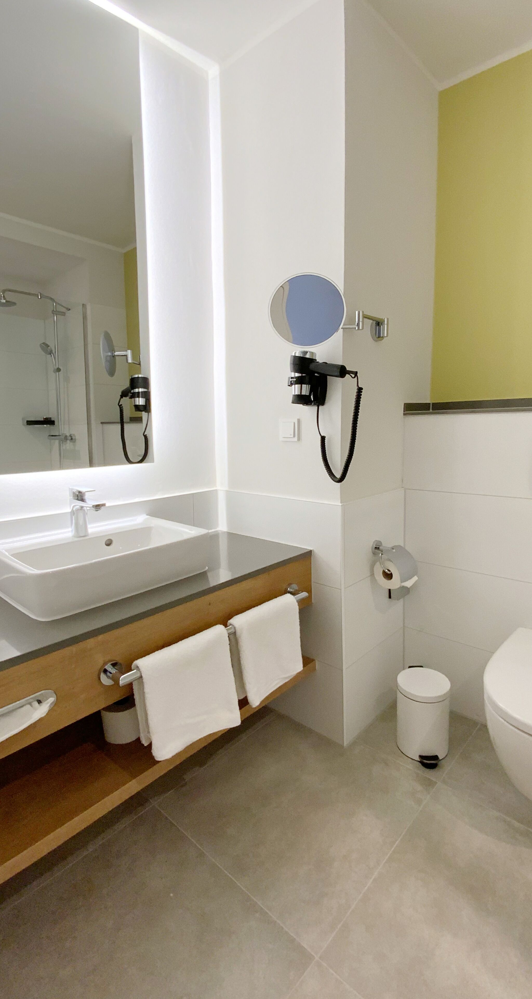 Un baño moderno con un espejo grande, un lavabo, un inodoro y una ducha.