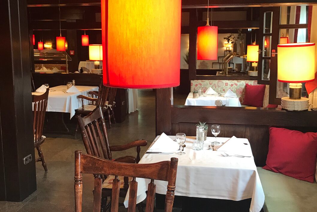 A restaurant interior with tables set for dining, wooden chairs, and red hanging lamps.
