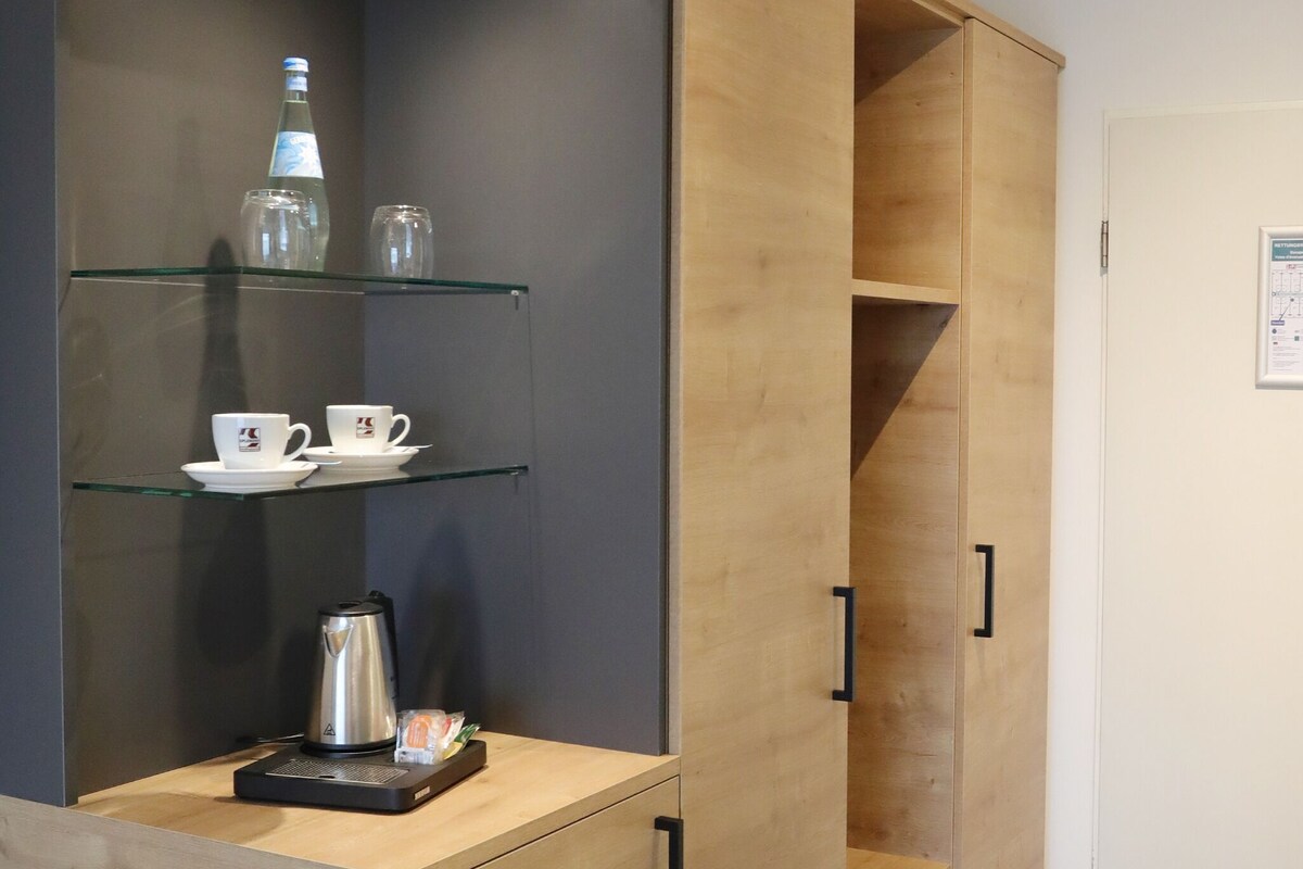 A modern kitchen with wooden cabinets, a coffee maker, and a kettle on the countertop.