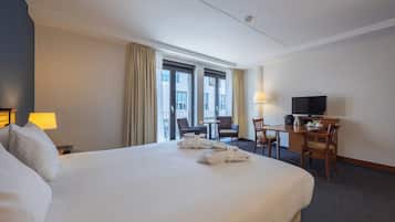 Ein Hotelzimmer mit einem großen Bett, einem Schreibtisch mit Stuhl, einem Fernseher und einem Fenster mit Vorhängen.