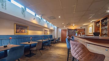 A restaurant with blue booths, wooden tables, and a bar area.