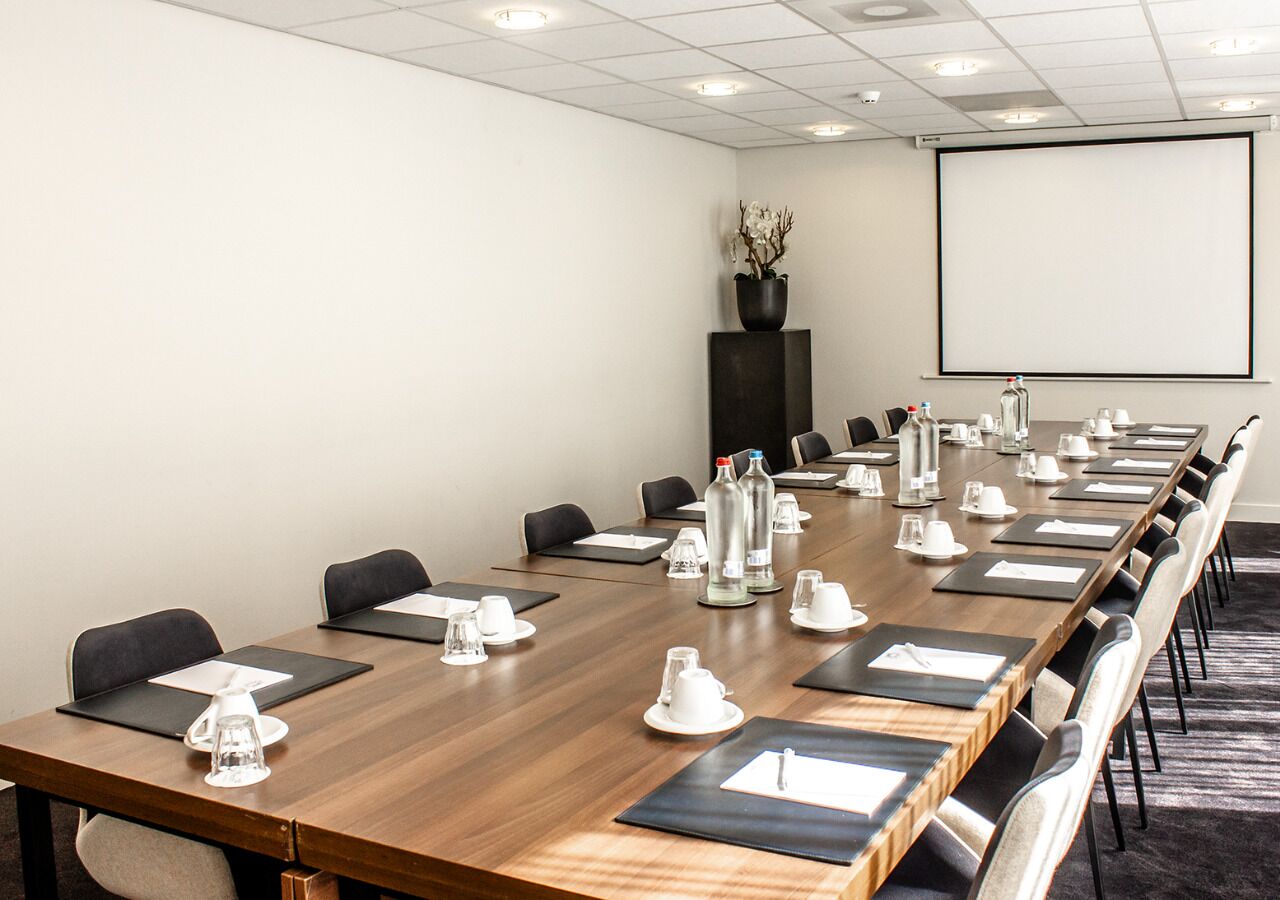 A conference room with a long table, chairs, water bottles, and a projector screen.