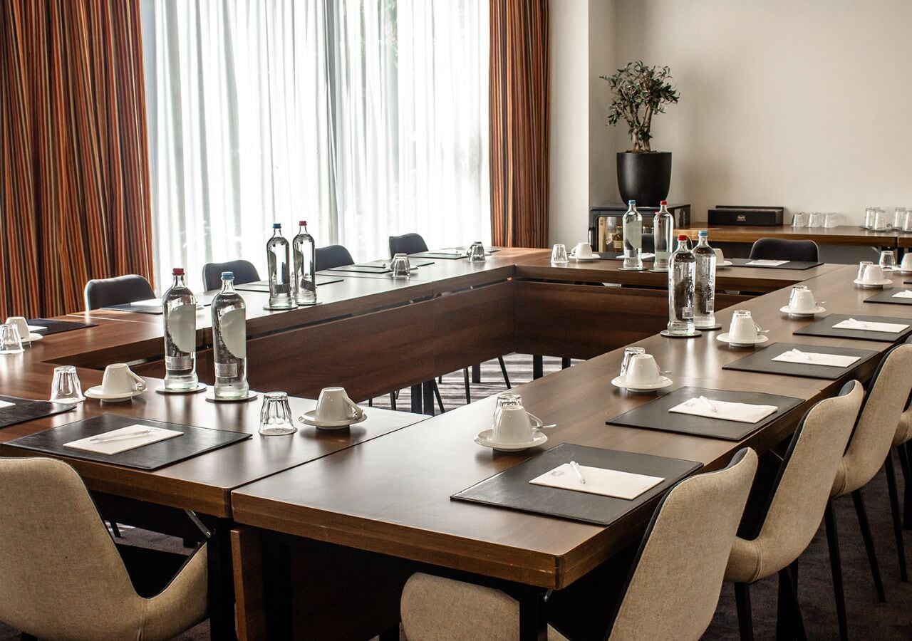 A conference room with a long table set for meetings, equipped with water bottles, glasses, and a potted plant.