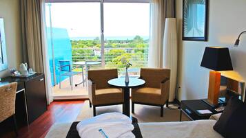 A hotel room with a bed, a desk, a chair, a small table, a lamp, and a view of the outdoors.