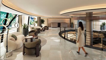 Een moderne lobby met een golvend ontwerp, met een zithoek met banken en fauteuils, een trap en een groot raam met uitzicht op groen.