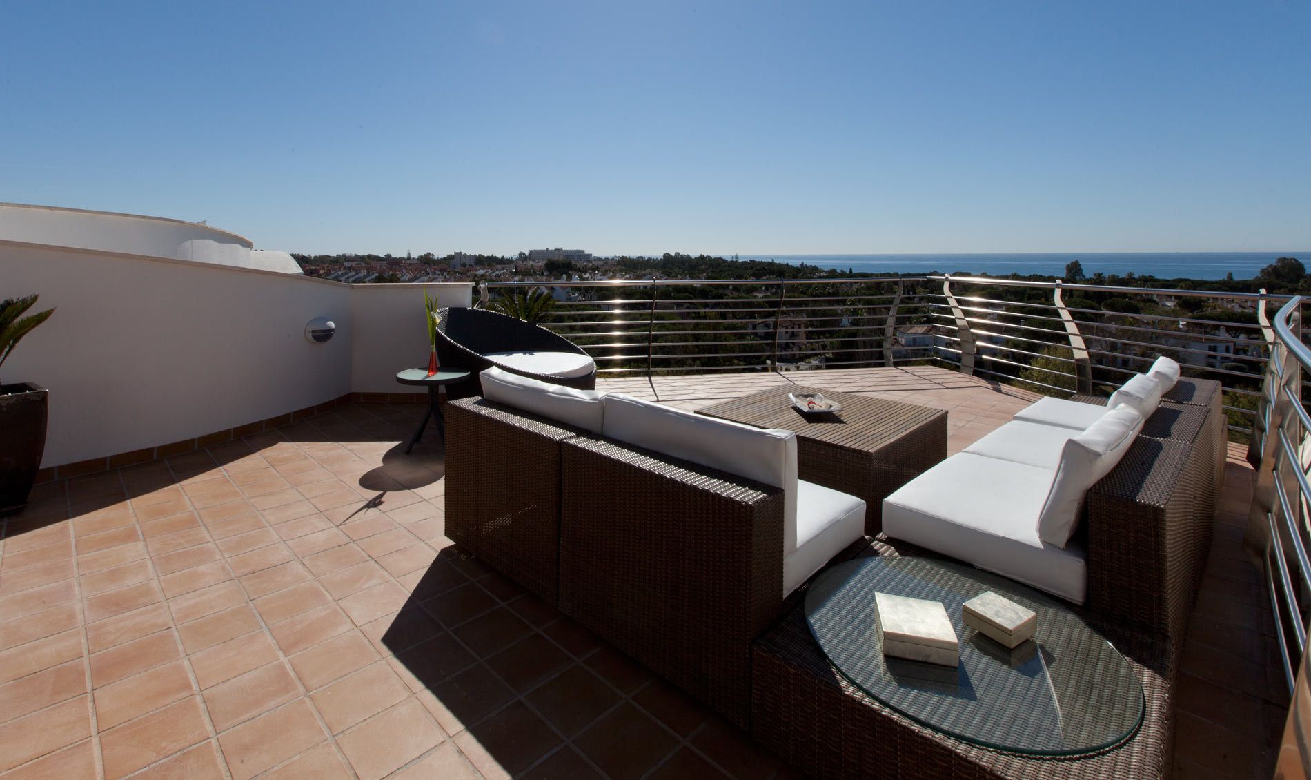 Una terraza en la azotea con mobiliario exterior, una mesa de vidrio y vista al mar.