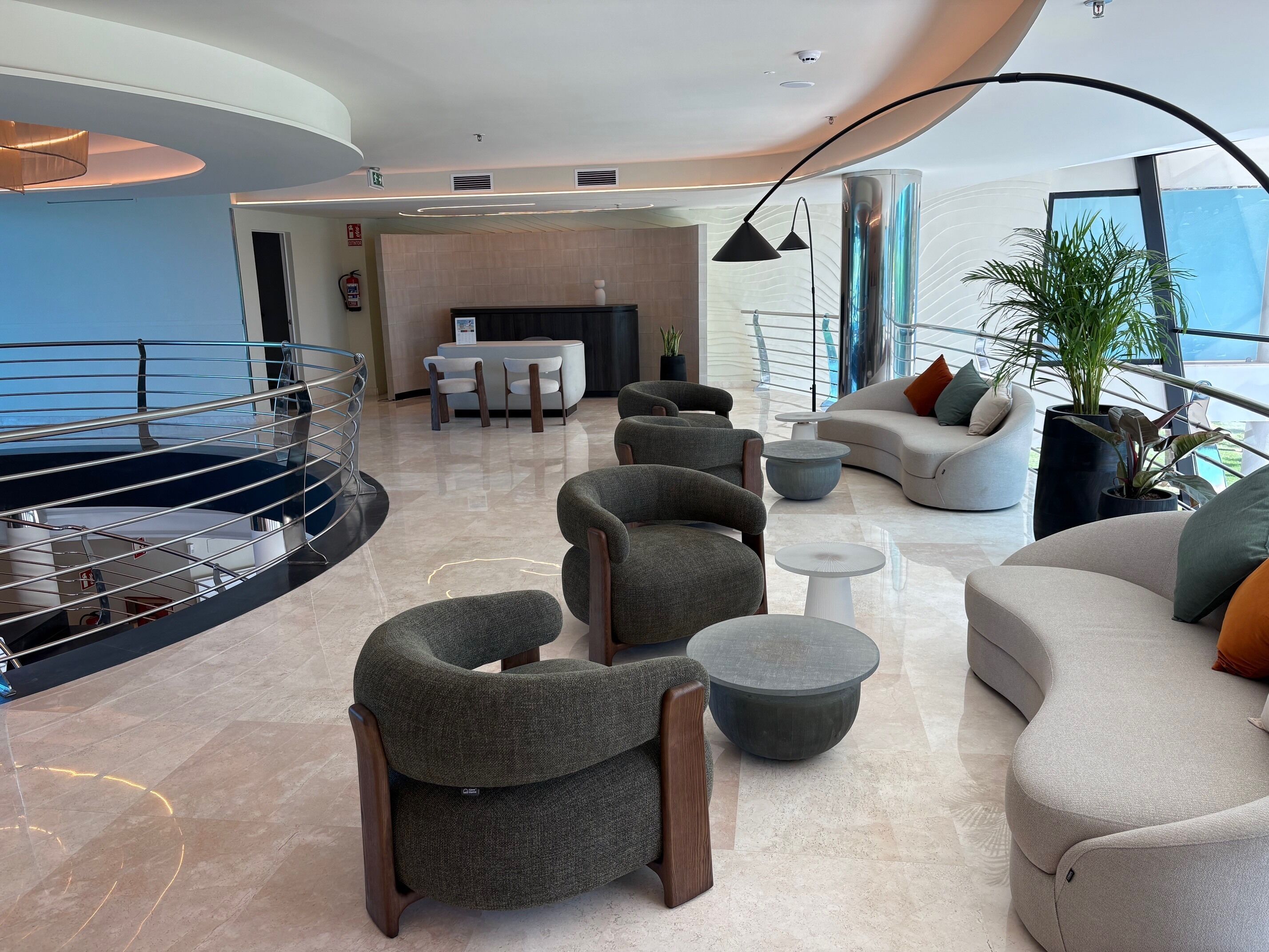 A modern hotel lobby with a curved railing, seating area, and a fireplace.