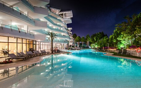 A swimming pool with lounge chairs and a modern building with multiple balconies.