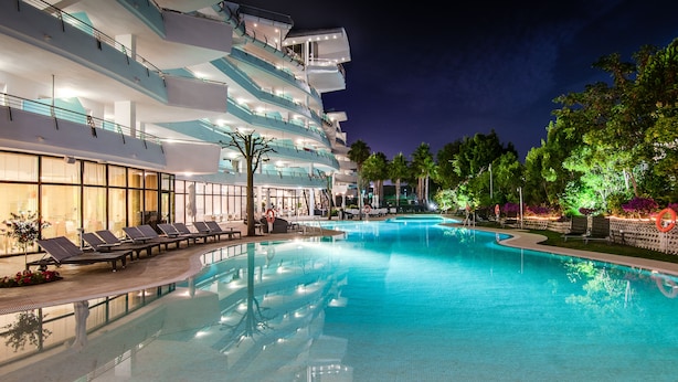 A swimming pool with lounge chairs and a modern building with multiple balconies.